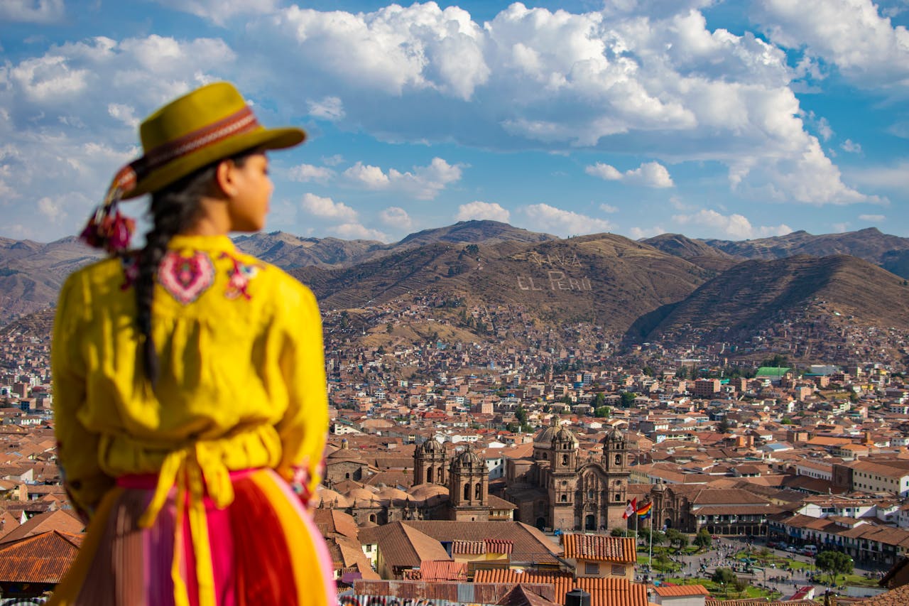 A woman in traditional clothing gazes at the stunning Cusco skyline, capturing Perus cultural essence.